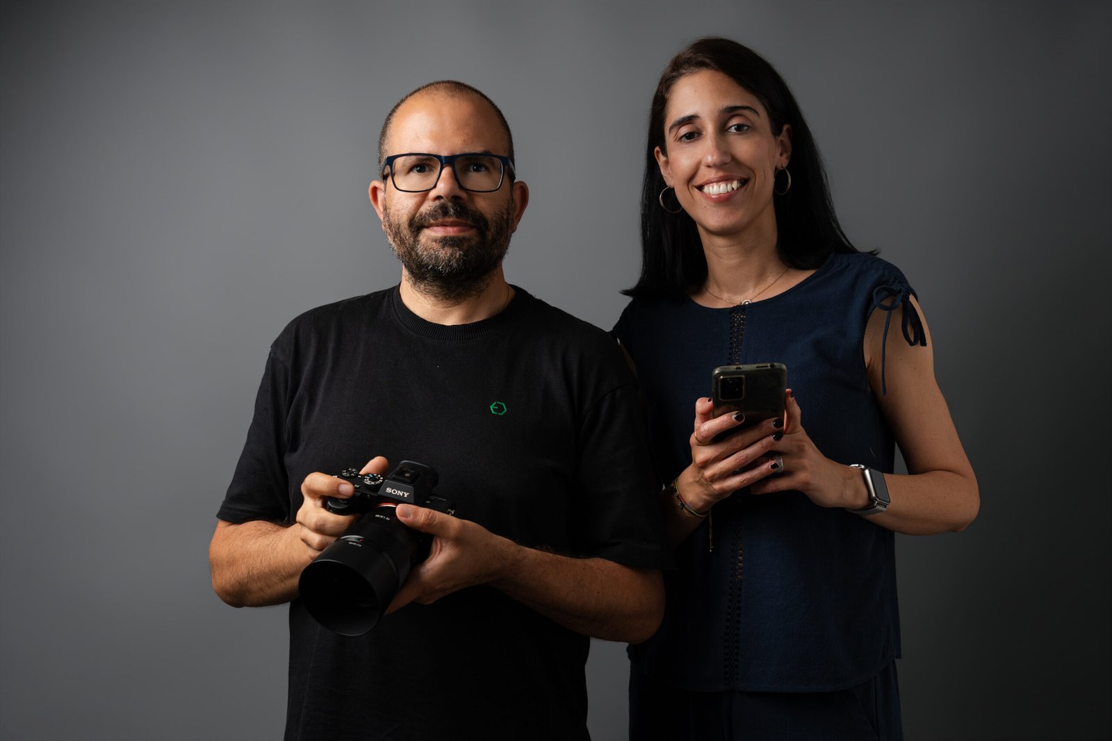 Sérgio - fotógrafo com máquina fotográfica na mãe e Andreia, gestora de marketing, com telemóvel na mão